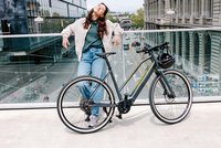 Light Support E-Bikes. Eine junge Frau lehnt lässig an einem Geländer.