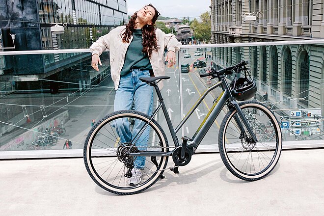 Light Support E-Bikes. Eine junge Frau lehnt lässig an einem Geländer.