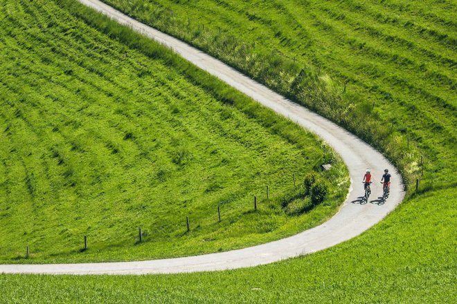 Zwei Radfahrer in einer langen Kurve inmitten grüner Natur.