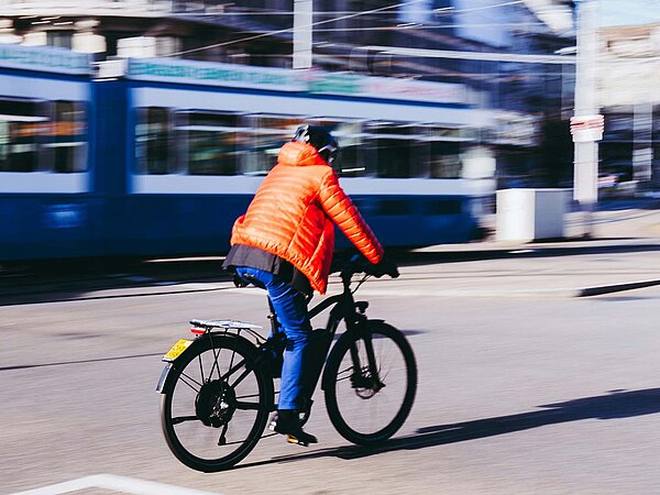 Avenir Suisse Studie Tempo ÖV Schweizer Städte. Eine Person mit oranger Jacke fährt in Zürich auf einem E-Bike.
