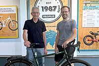 Veloplus Verwaltungsrat Wechsel an der Spitze. Zwei Männer stehen hinter einem Fahrrad.