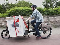 Mann transportiert Waschmaschine mit Lastenrad. Bonus für Cargobikes. 