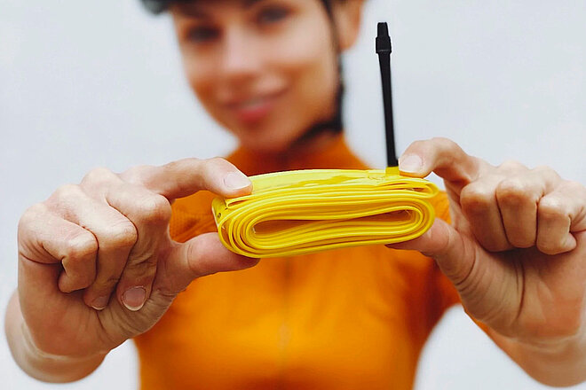Eine Rennradfahrerin mit gelbem Tricot hält einen gelben, leichten Fahrradschlauch von Pirelli in der Hand