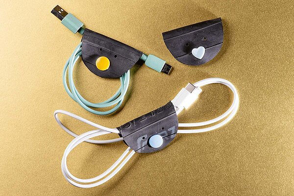 Kabelhalter aus Veloschlauch mit bunten Knöpfen auf goldenem Untergund.