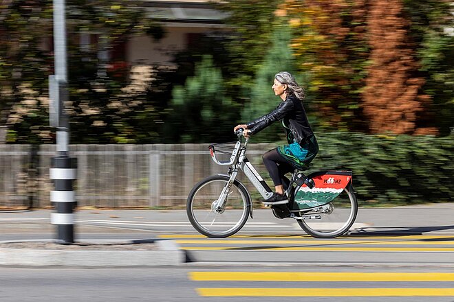 Eine Frau mit grauen Haaren fährt auf einem Fahrrad in der Stadt.