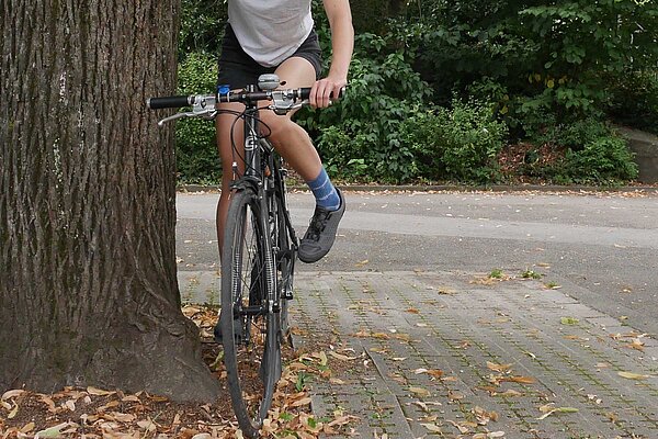 Tipps und Tricks für Klickpedale. Eine Frau hält sich auf dem Velo an einem Baum fest.