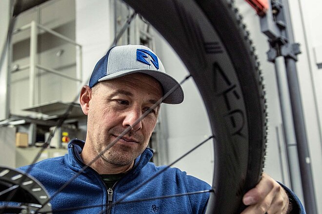 Ein Mann mit Schirmmütze inspiziert das Laufrad eines Velos.