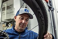 Ein Mann mit Schirmmütze inspiziert das Laufrad eines Velos.