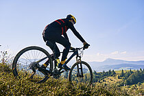 Mountainbiker fährt über Hügelkamm mit Bergen im Hintergund