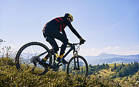 Mountainbiker fährt über Hügelkamm mit Bergen im Hintergund