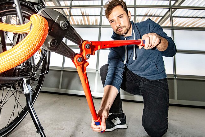 Fahrradschloss Test. Die besten Veloschlösser. Ein Mann knack ein Fahrradschloss mit einer Zange.