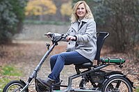 blonde Frau fährt auf Dreirad auf einem Waldweg