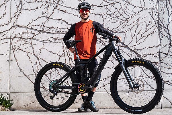 Ein Biker steht mit Bikebekleidung und Helm hinter seinem Mountainbike
