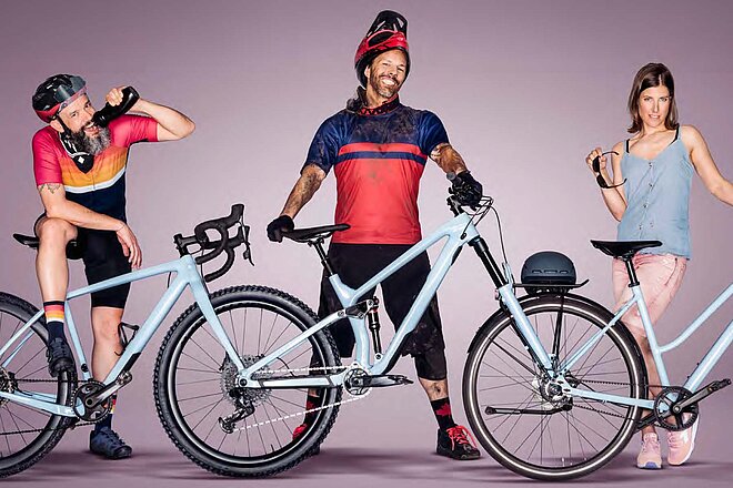 Drei Personen, zwei Männer und eine Frau, posieren mit hellblauen Fahrrädern vor einem violetten Hintergrund.